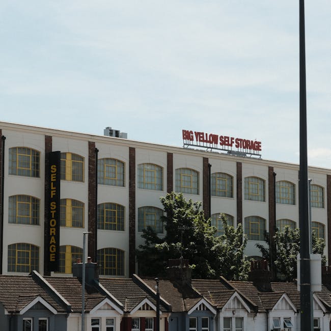 The image shows a multi-storey commercial building with a sign reading 'BIG YELLOW SELF STORAGE' on the roof and another vertical sign indicating 'SELF STORAGE' on the side, with a clear sky overhead.